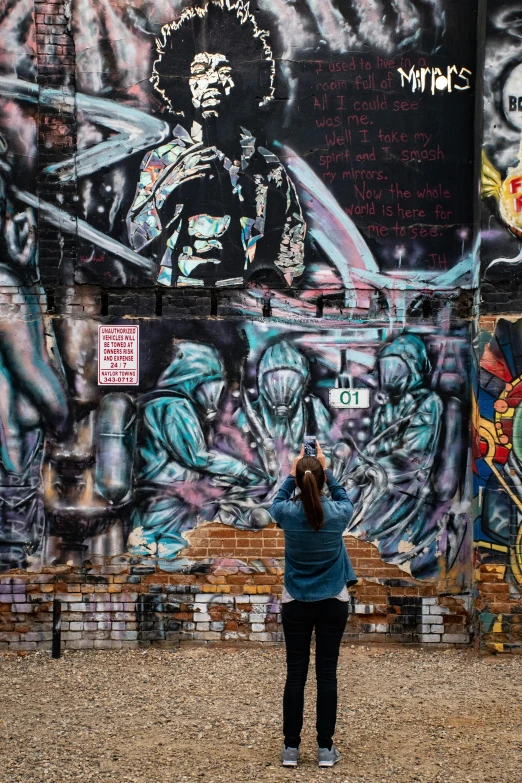 a woman standing in front of a wall covered in graffiti, graffiti art, inspired by Tim Okamura, pexels contest winner, cleveland, photographed from the back, taking a picture, australia