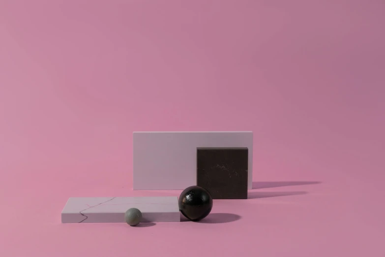 a black and white object sitting on top of a pink surface, an abstract sculpture, inspired by Harvey Quaytman, postminimalism, chocolate candy bar packaging, flying black marble balls, obsidian pomegranade, smooth solid concrete