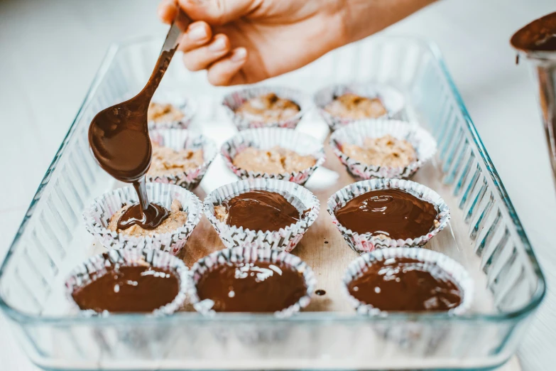 a person scooping chocolate into a tray of cupcakes, by Nicolette Macnamara, trending on pexels, homemade, 🦩🪐🐞👩🏻🦳, wet boody, brunette