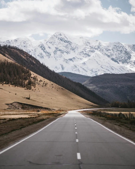 an empty road with mountains in the background, by Anna Haifisch, unsplash contest winner, photo of putin, snowy peaks, grey, with rolling hills