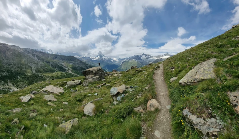 a dirt path on a grassy hill with a mountain in the background, by Werner Andermatt, pexels contest winner, les nabis, panorama view of the sky, standing on rocky ground, with lots of vegetation, ben ridgway