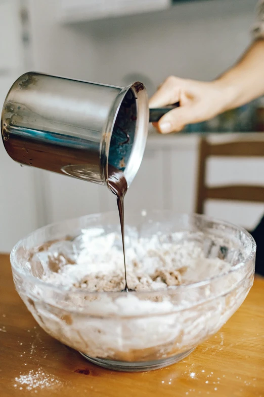 a person pouring something into a bowl on a table, powdered sugar, thumbnail, dwell, chocolate frosting