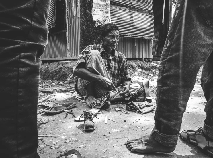 a black and white photo of a man sitting on the ground, by Bikash Bhattacharjee, pexels contest winner, tools and junk on the ground, shoes, sculptor, assamese