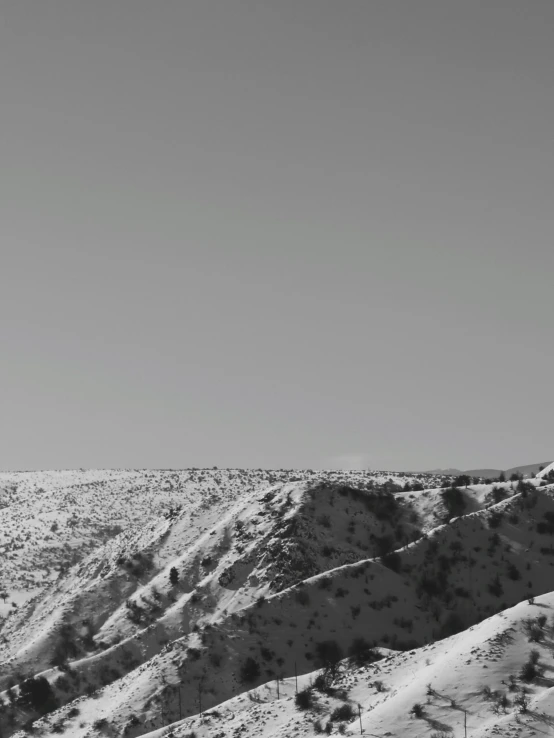 a black and white photo of a snow covered mountain, a black and white photo, unsplash, agrigento, background image, hillside, the planet is warm with canyons