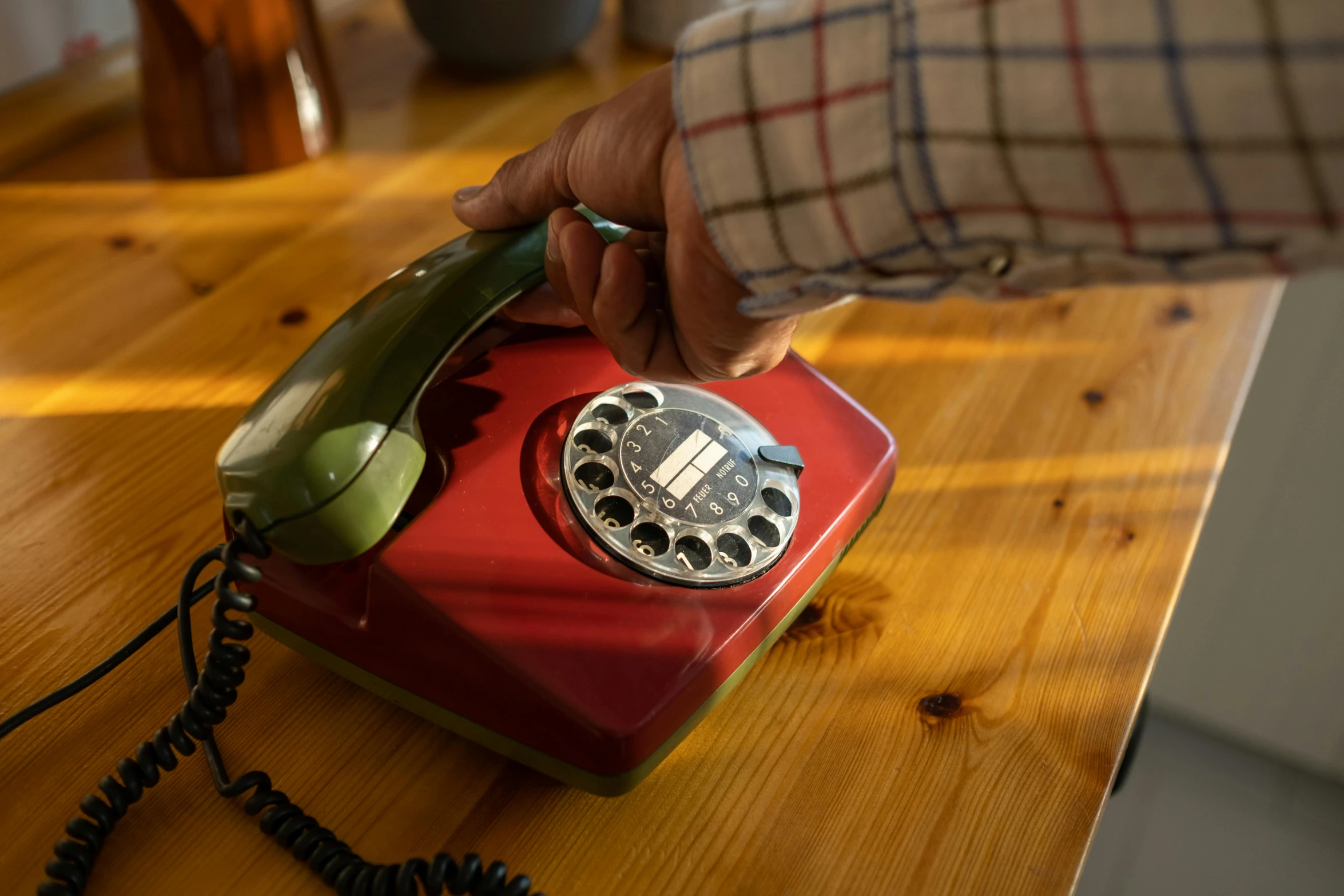 a red telephone sitting on top of a wooden table, back of hand on the table, red and green, from the 7 0 s, customers