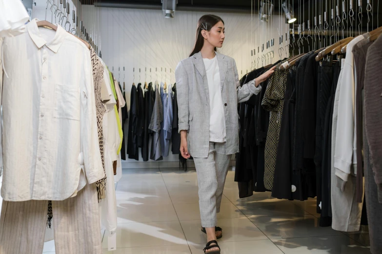 a woman standing in front of a rack of clothes, grey suit, wearing a linen shirt, soami, grand finale