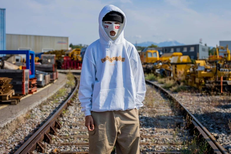 a man in a white hoodie standing on a train track, a portrait, unsplash, graffiti, outlive streetwear collection, 🍂 cute, white mask, oversized hoodie