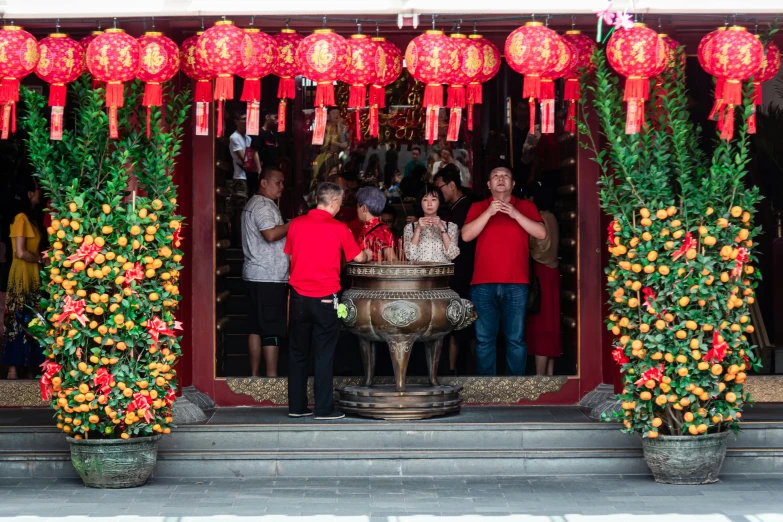 a group of people standing in front of a building, red adornments, tea drinking and paper lanterns, 2019 trending photo, singapore