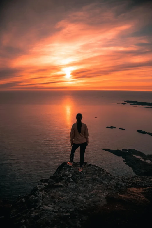 a person standing on a rock overlooking the ocean at sunset, by Jesper Knudsen, pexels contest winner, nina tryggvadottir, gazing off into the horizon, minn, overlooking