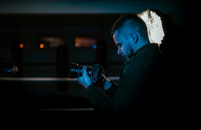 a man holding a gun in the dark, a picture, by Adam Marczyński, pexels contest winner, holding a big camera, medium format. soft light, profile picture 1024px, indoor picture