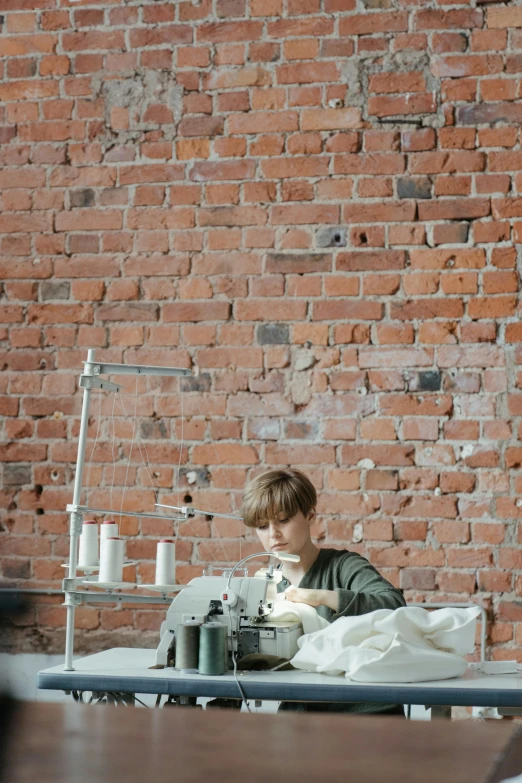 a woman sitting at a sewing machine in front of a brick wall, work clothes, anton fadeev 8 k, production photo, inspect in inventory image