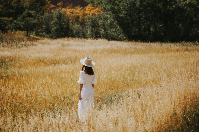 a woman walking through a field of tall grass, unsplash contest winner, white cowboy hat, full body white dress, fall season, background image