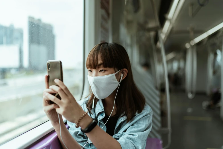 a woman wearing a face mask looking at her phone, a picture, trending on pexels, square, sat down in train aile, chinese girl, avatar image