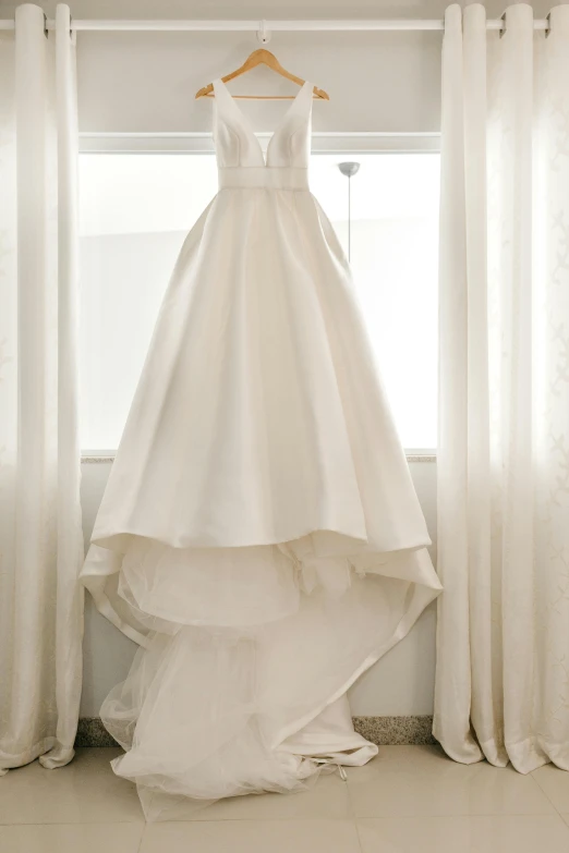 a wedding dress hanging in front of a window, no - text no - logo, white backdrop, up-close, jen atkin