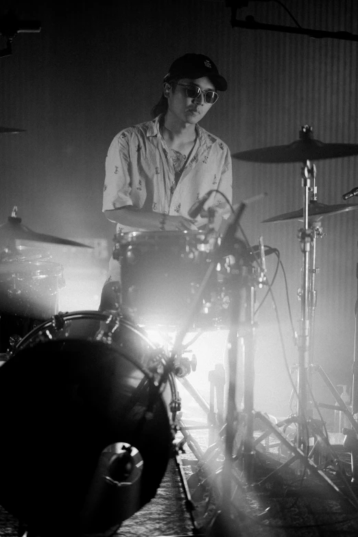 a black and white photo of a man playing drums, warpaint aesthetic, with sunglass, syd, lights