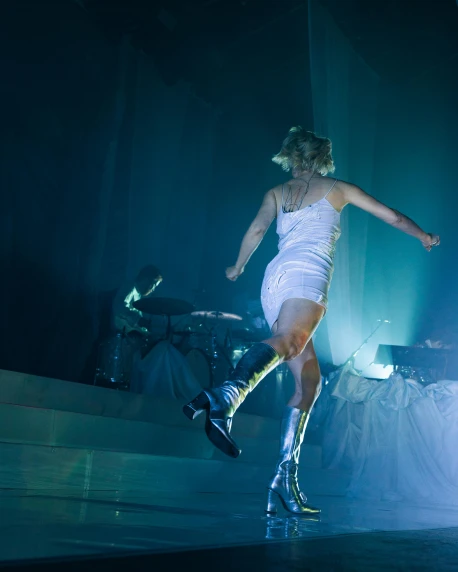 a woman in a white dress is dancing on stage, inspired by Nan Goldin, unsplash, happening, wearing skirt and high socks, beth cavener, on an icy throne, high quality photo