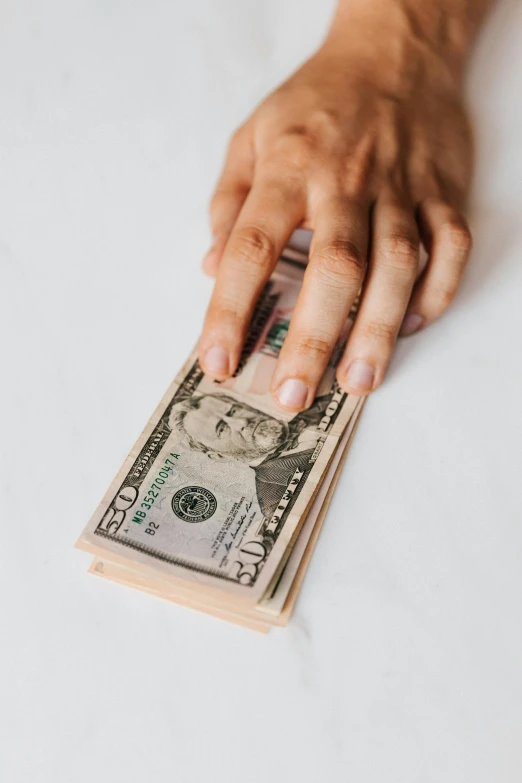 a woman's hand holding a stack of one hundred dollar bills, by Byron Galvez, pexels contest winner, on a white table, thumbnail, 1 8, plain background