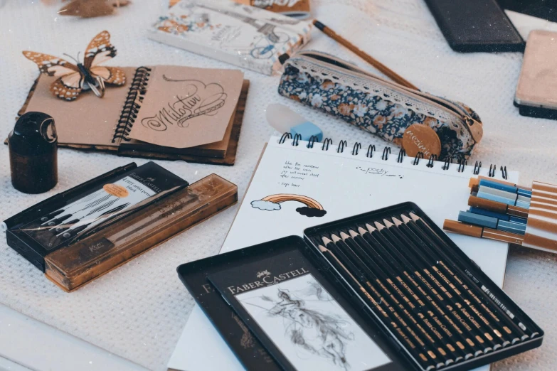 a table topped with lots of different colored pencils, a drawing, by Andrée Ruellan, pexels contest winner, black and brown colors, lacey accessories, caligraphy, sketch book