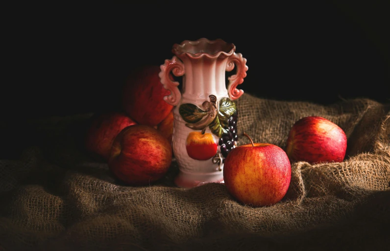 a white vase sitting on top of a table next to apples, by Adam Marczyński, pexels contest winner, pink and red colors, antique piece, an artistic pose, red and orange colored