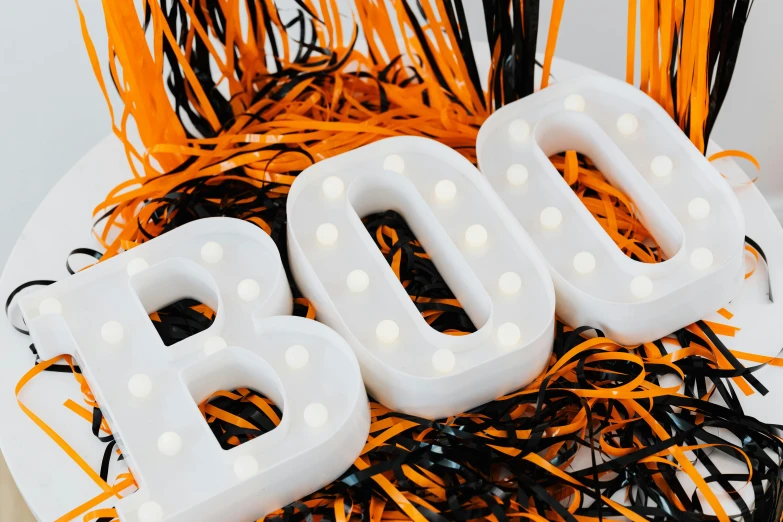 a white sign sitting on top of a pile of black and orange streamers, by Joe Bowler, trending on unsplash, beistle halloween decor, skin made of led point lights, close up front view, bubble letters