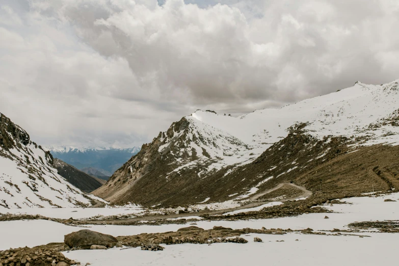 a man riding a snowboard down a snow covered slope, pexels contest winner, breathtaking himalayan landscape, background image, road between hills, grey cloudy skies