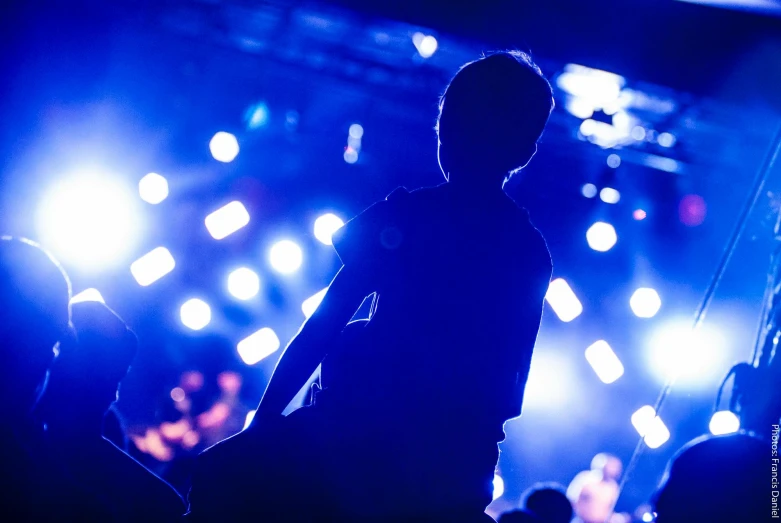 a silhouette of a person standing in front of a stage, unsplash, happening, party lights, blue lights, teenage boy, tight shot of subject