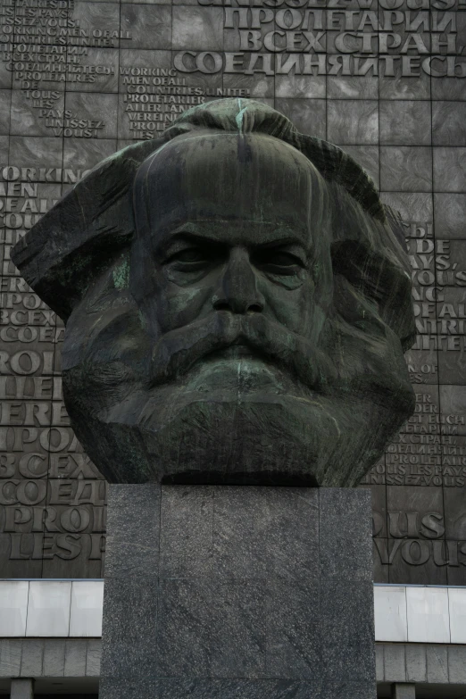 a statue of a man with a beard in front of a building, karl marx, dark grey haired man, square face, center of image