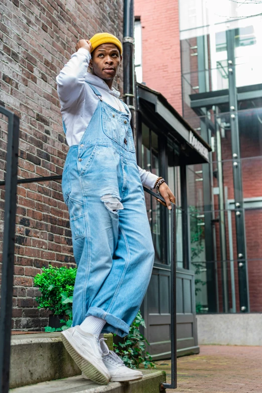 a man in overalls leaning against a pole, an album cover, trending on pexels, happening, baggy jeans, afropunk, doing a sassy pose, ::