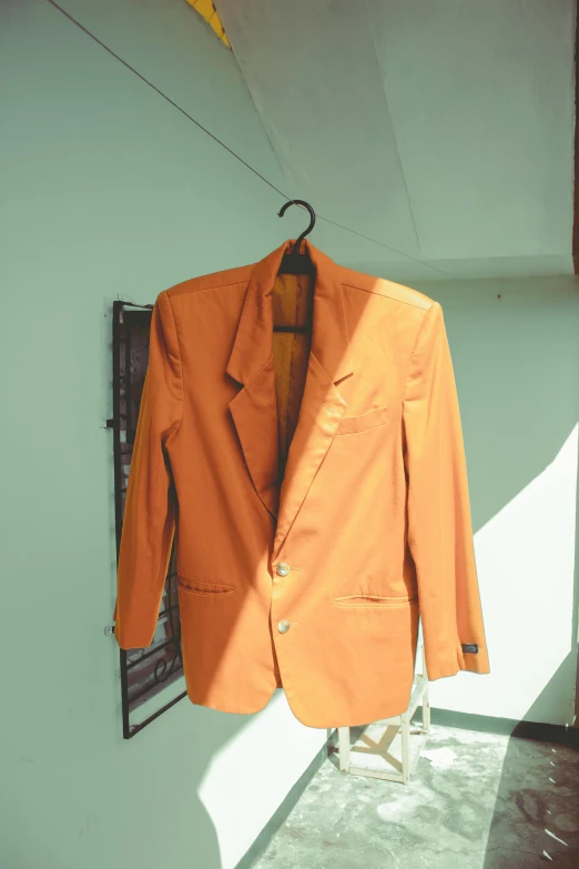 an orange jacket hanging on a wall next to a window, wearing a worn out brown suit, early 2 0 0 0 s, slightly sunny, display item