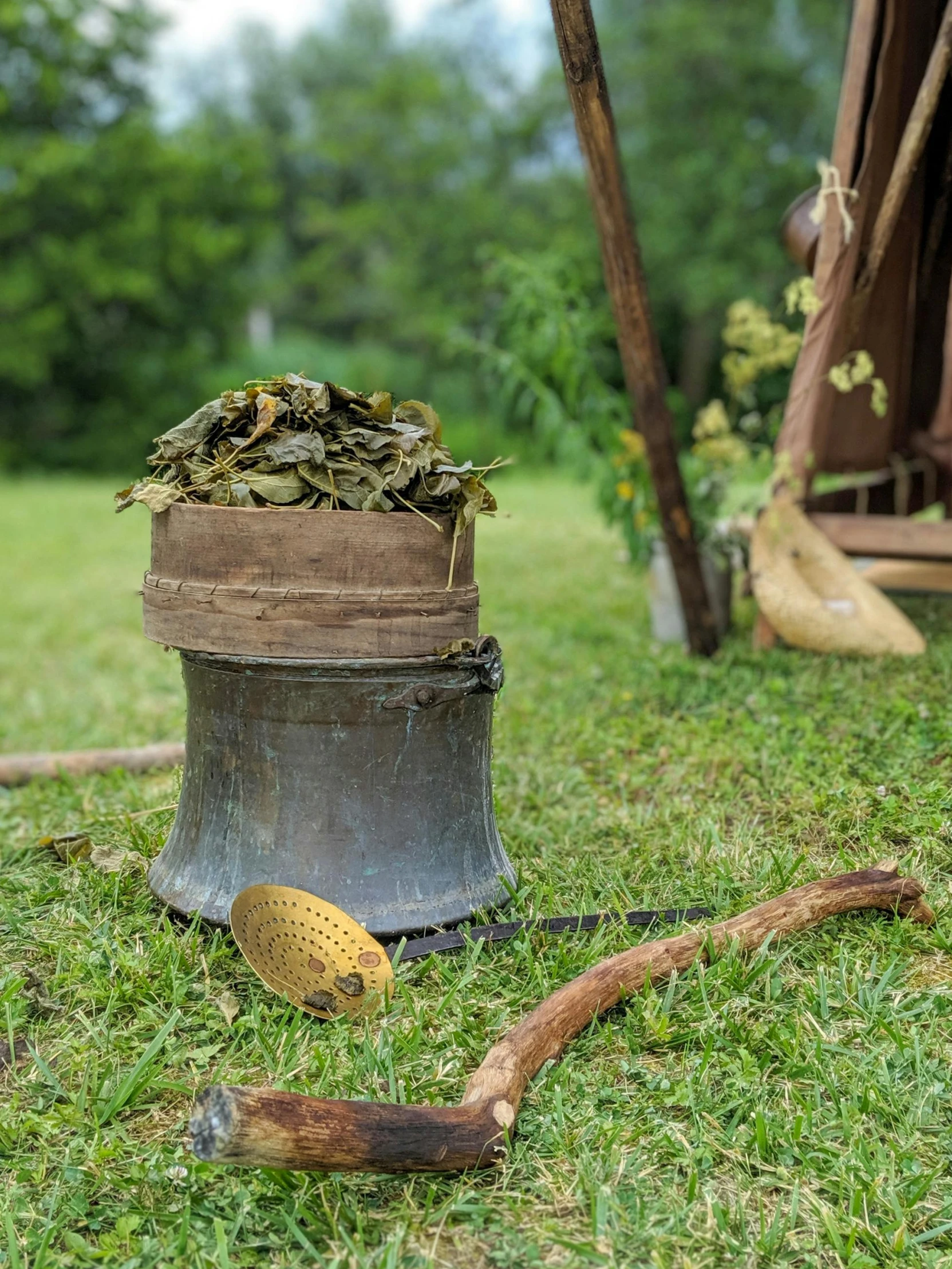 a bucket filled with leaves sitting on top of a lush green field, land art, holding a golden bell, brass debris, old english garb, with a wooden stuff