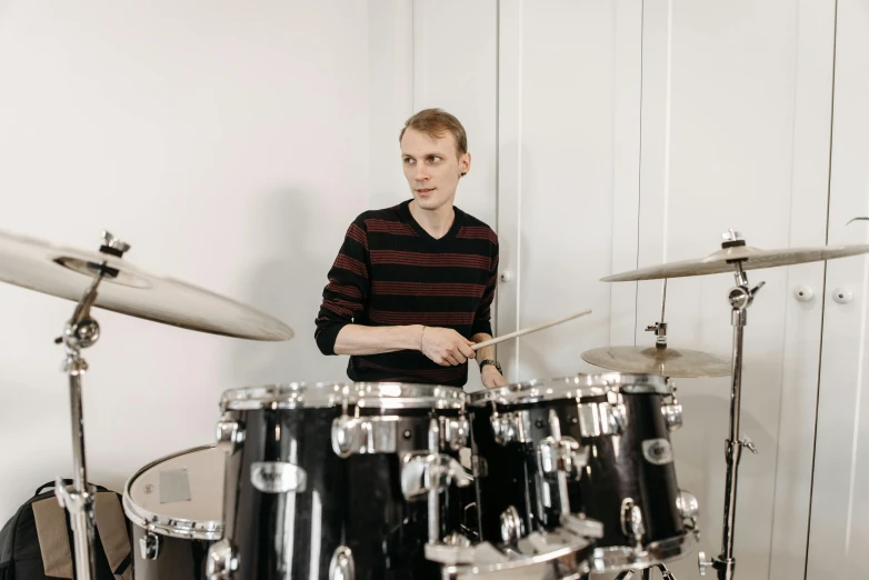 a man sitting in front of a drum set, inspired by Alexander Kanoldt, pexels contest winner, realism, vitalik buterin, on a pale background, performing, avatar image