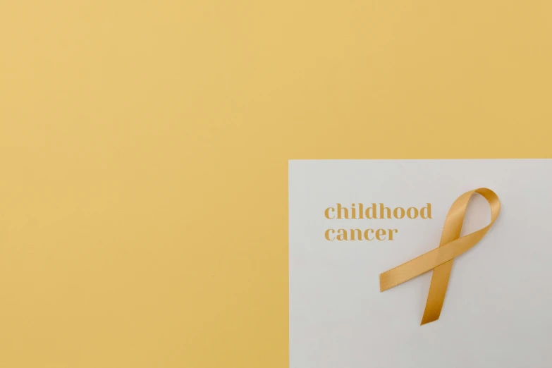 a piece of paper with a gold ribbon on it, by Emma Andijewska, pexels contest winner, the cure for cancer, children's toy, childish gambino, colors: yellow