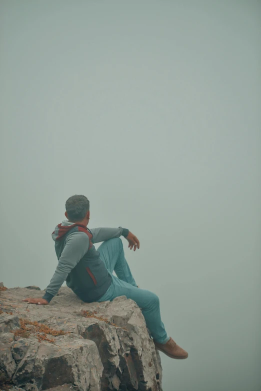 a man sitting on top of a large rock, by Attila Meszlenyi, trending on unsplash, romanticism, cyan fog, looking exhausted, gray men, teal aesthetic