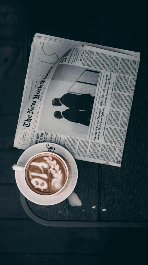 a newspaper sitting on top of a table next to a cup of coffee, a black and white photo, by Nyuju Stumpy Brown, pexels contest winner, detailed photo of an album cover, 15081959 21121991 01012000 4k, latte art, instagram photo