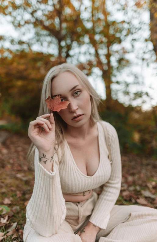 a woman sitting on the ground with a leaf in her hand, an album cover, trending on pexels, sydney sweeney, intense albino, headshot profile picture, autum