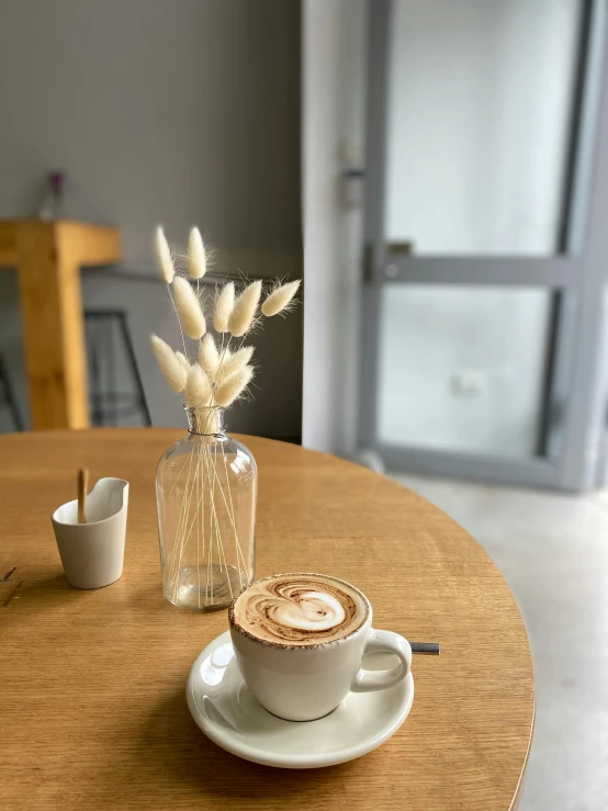 a cup of coffee sitting on top of a wooden table, thumbnail, taken on iphone 1 3 pro, cafe interior, full body image