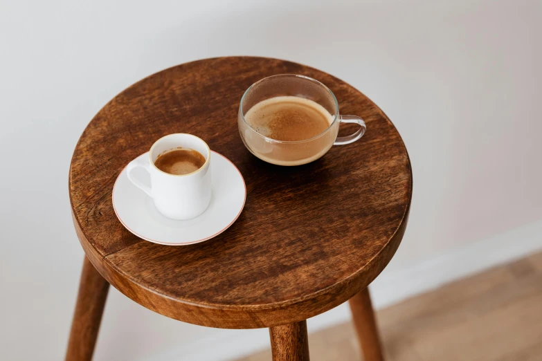 a cup of coffee sitting on top of a wooden table, jen atkin, stools, two cups of coffee, uncropped