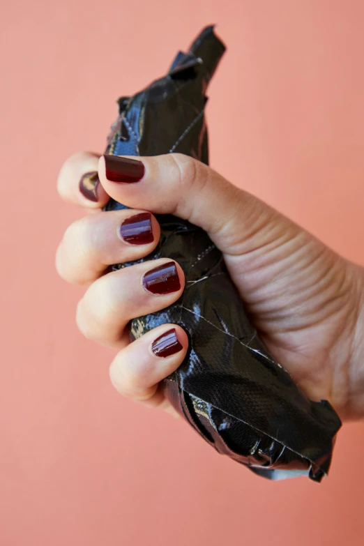 a person holding a banana in their hand, by Olivia Peguero, dark red and black color palette, cracked plastic wrap, neat nails, jen atkin