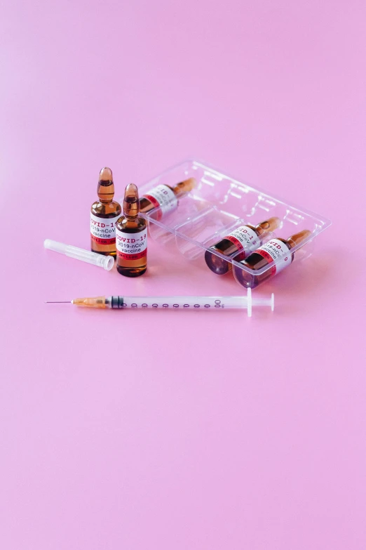 a syll and two vials on a pink background, by Julia Pishtar, pexels, syringe, left eye red stripe, on a white table, fujicolor sample