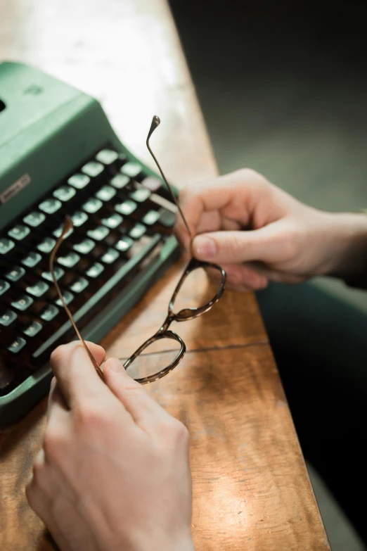 a close up of a person typing on a typewriter, a portrait, trending on pexels, small square glasses, vintage muted colors, hero shot, teaching