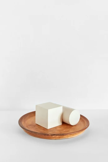 a small white block sitting on top of a wooden plate, an abstract sculpture, inspired by Isamu Noguchi, round-cropped, various sizes, butter sculpture, full product shot