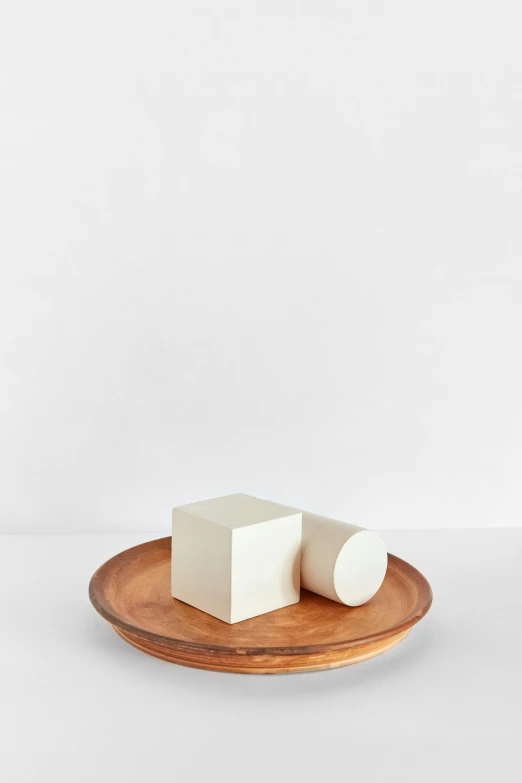 a small white block sitting on top of a wooden plate, an abstract sculpture, inspired by Isamu Noguchi, round-cropped, various sizes, butter sculpture, full product shot