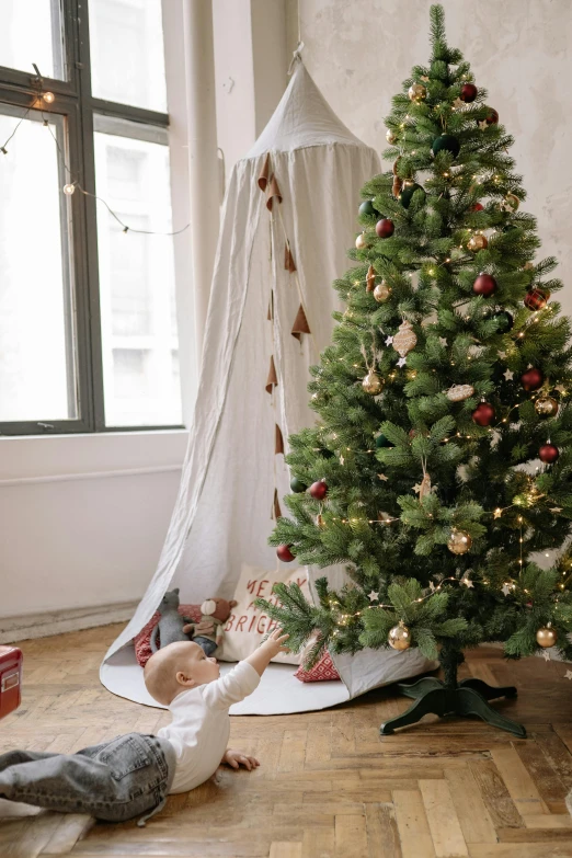 a baby laying on the floor next to a christmas tree, by Julia Pishtar, renaissance, ethereal curtain, in a white boho style studio, gif, abcdefghijklmnopqrstuvwxyz