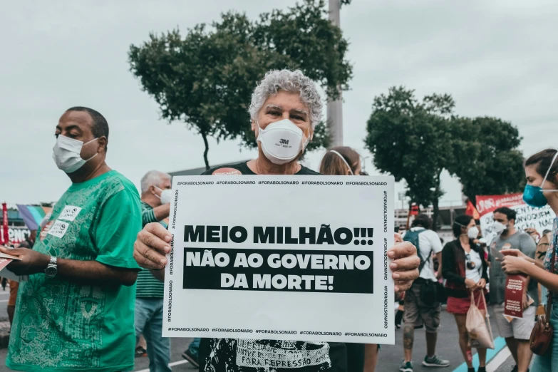 a man in a face mask holding a sign, by João Artur da Silva, instagram post, photo taken in 2018, no watermarks, death and corruption