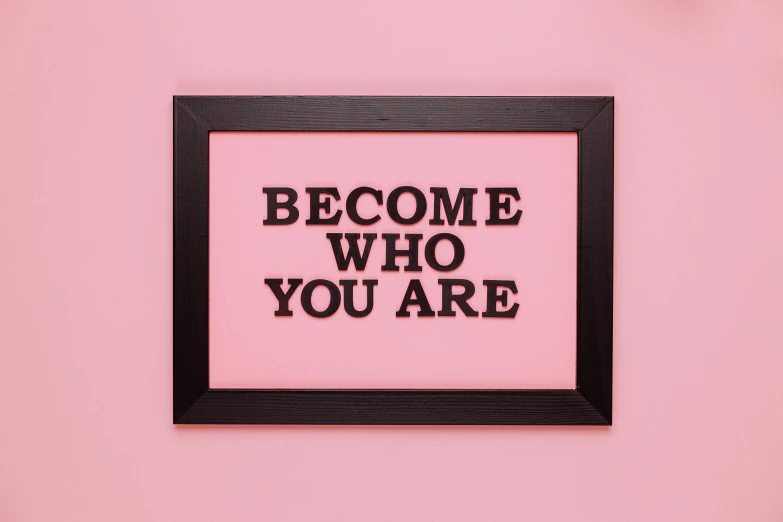 a pink wall with a black frame that says become who you are, a picture, pexels, folk art, brown, black, bronze, rectangle
