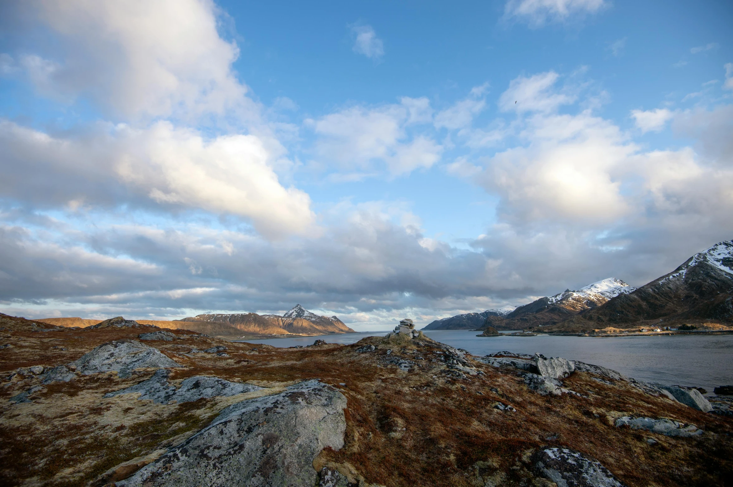 a large body of water sitting on top of a grass covered hillside, inspired by Johan Christian Dahl, unsplash, snowy fjord, thumbnail, ceremonial clouds, rocky terrain