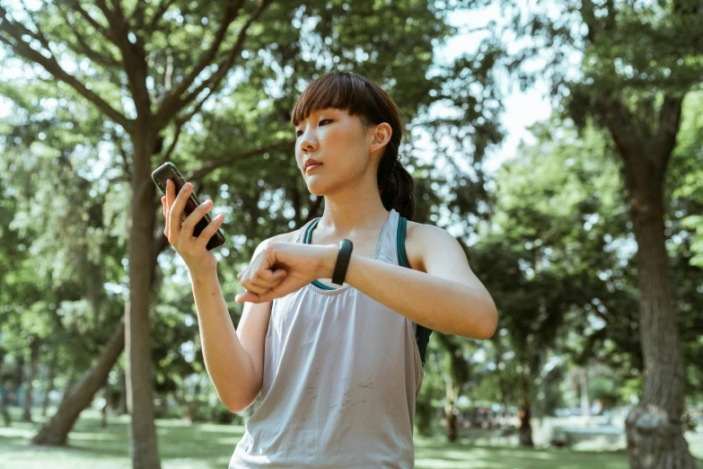 a woman standing in a park looking at her cell phone, pexels, realism, wearing fitness gear, asian features, square, improvisational