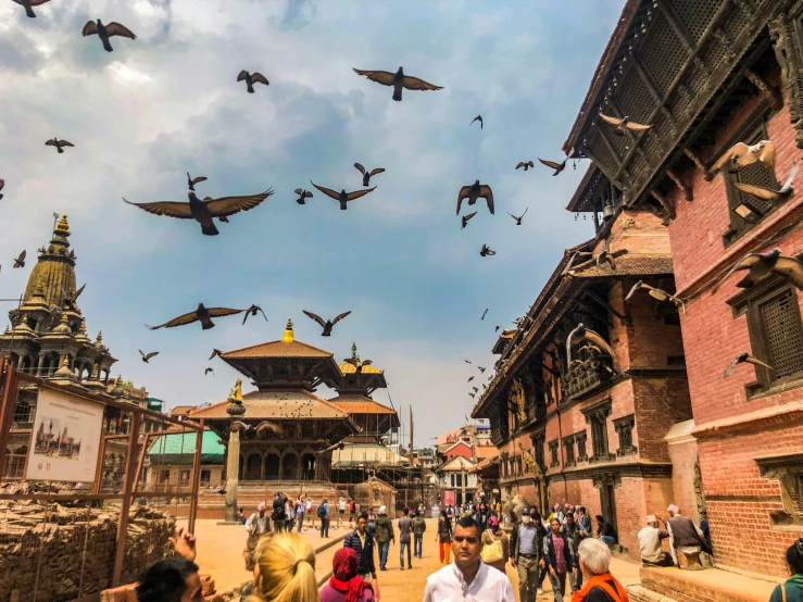 a group of people walking down a street next to tall buildings, inspired by Steve McCurry, pexels contest winner, hurufiyya, nepal, many birds and roses fly around, peaked wooden roofs, a wide open courtyard in an epic