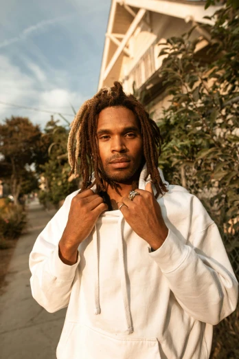 a man with dreadlocks standing in front of a house, an album cover, trending on pexels, wearing a white sweater, clement hurd, portrait shot 8 k, 15081959 21121991 01012000 4k