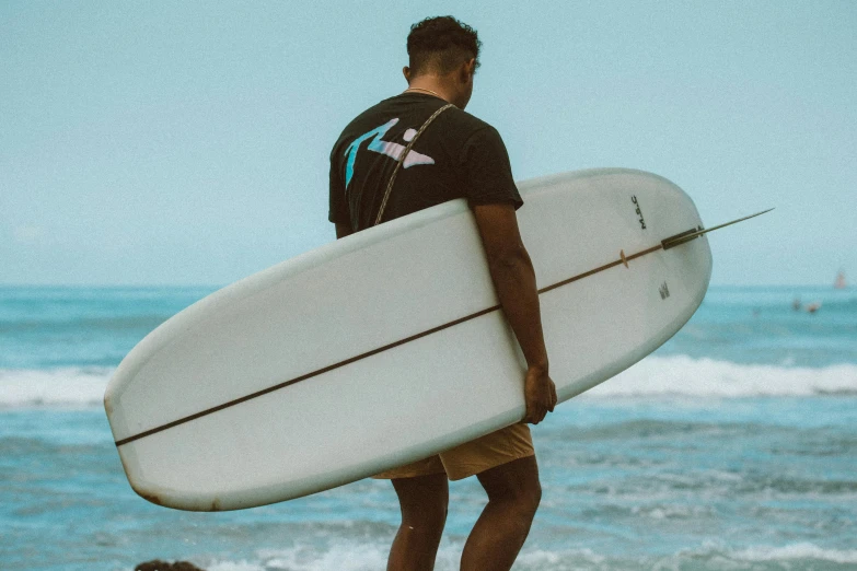 a man standing on a beach holding a surfboard, thick tail, streetwear, zoomed out, background image